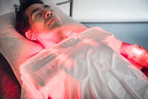 Man resting on a treatment table with a red light therapy pad across his chest
