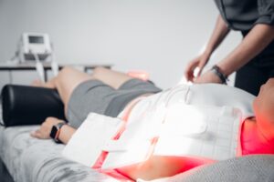 Practitioner adjusting LED therapy pads on a client lying face down on a treatment table