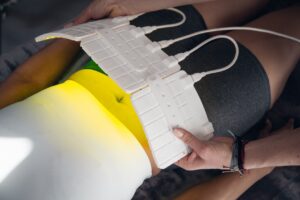 Practitioner adjusting a white LED pad wrapped around a client's waist, glowing green and yellow