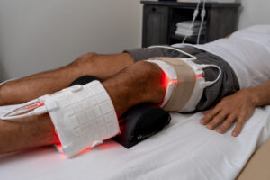 Leg resting on a bolster with an LED light therapy pad wrapped around the knee