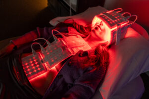 Woman lying under glowing red LED pads on her head and torso during a PBM session