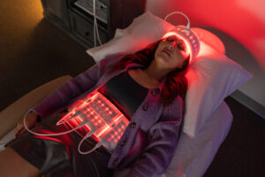 Woman lying down with red light therapy pads on her head and abdomen