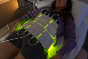 Woman in a purple cardigan lying down with LED pads across her abdomen glowing green