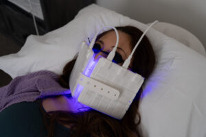 Woman lying on a pillow with an LED pad over her face glowing blue and violet