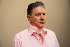 Man in a pink shirt wearing a white LED light therapy wrap around his neck