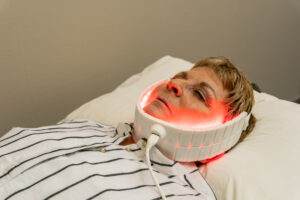 Woman lying down with a red-glowing LED wrap around her neck and jaw