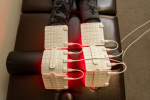 Both knees wrapped in white LED pads glowing red during a light therapy session