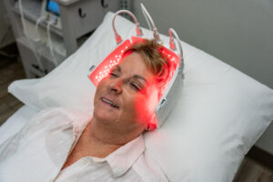 Smiling older woman lying on a pillow with a red LED light therapy cap on her head